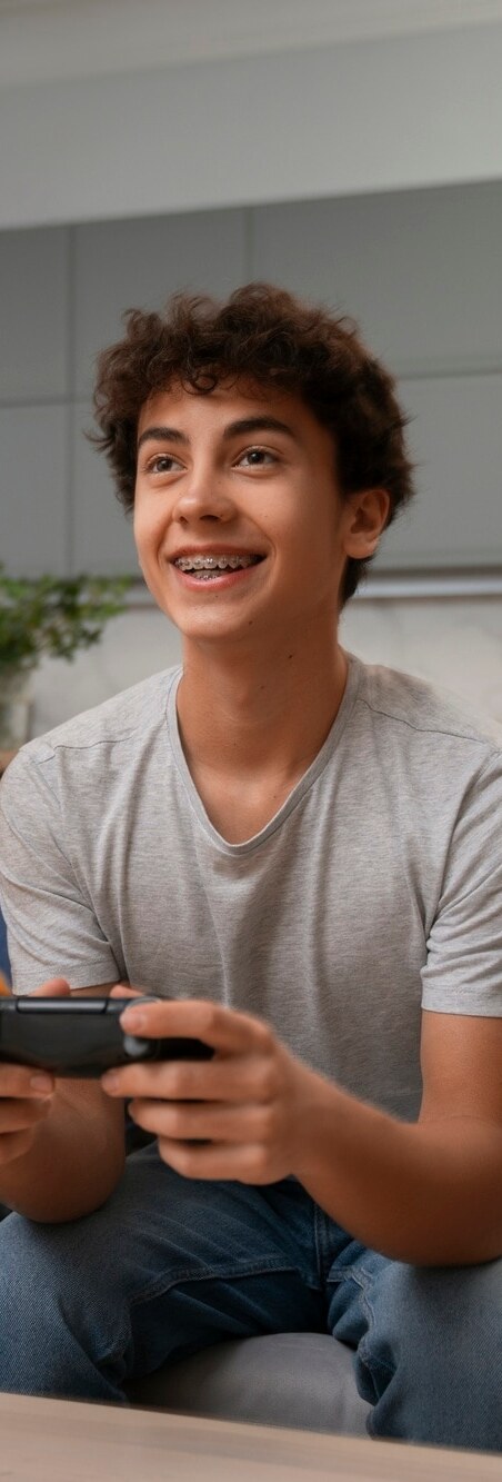 Chico joven con brackets sonriendo en el sofá de casa Joven sonriendo con brackets: ortodoncia en Clínica Dental Ziortza Ugarte, Donostia