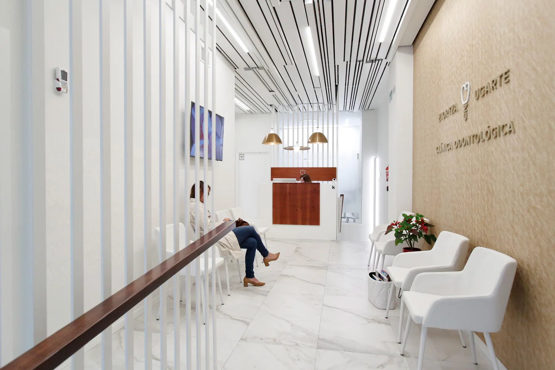 Recepción y pasillo de la clínica dental con listones blancos y pared dorada