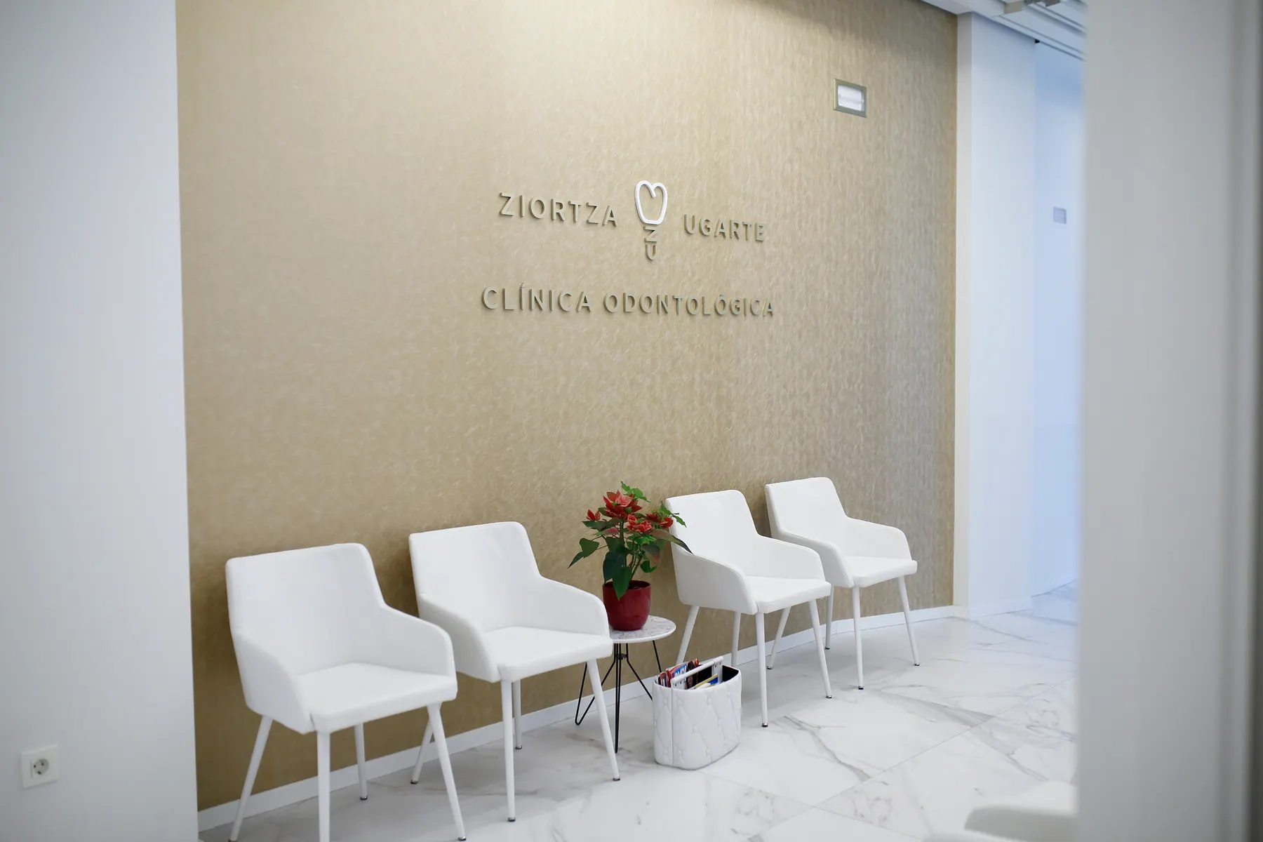 Sala de espera con sillones blancos y pared dorada con el logotipo